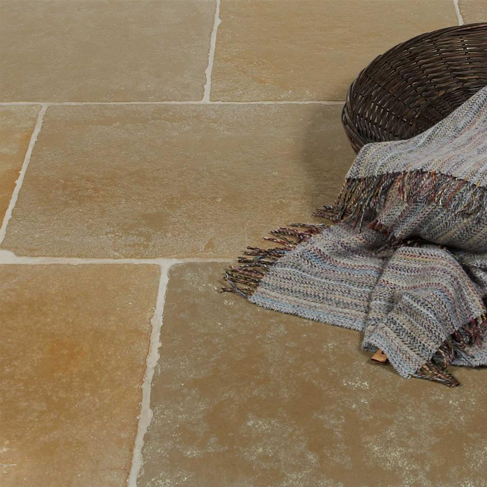 A close-up of chipped, beige limestone floor tiles